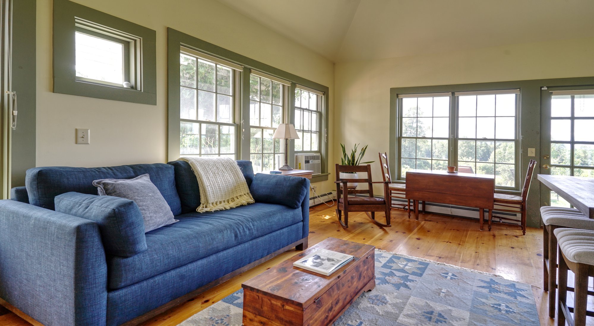 Blue sofa and antique drop-leaf table in the living area, surrounded by windows on two sides.