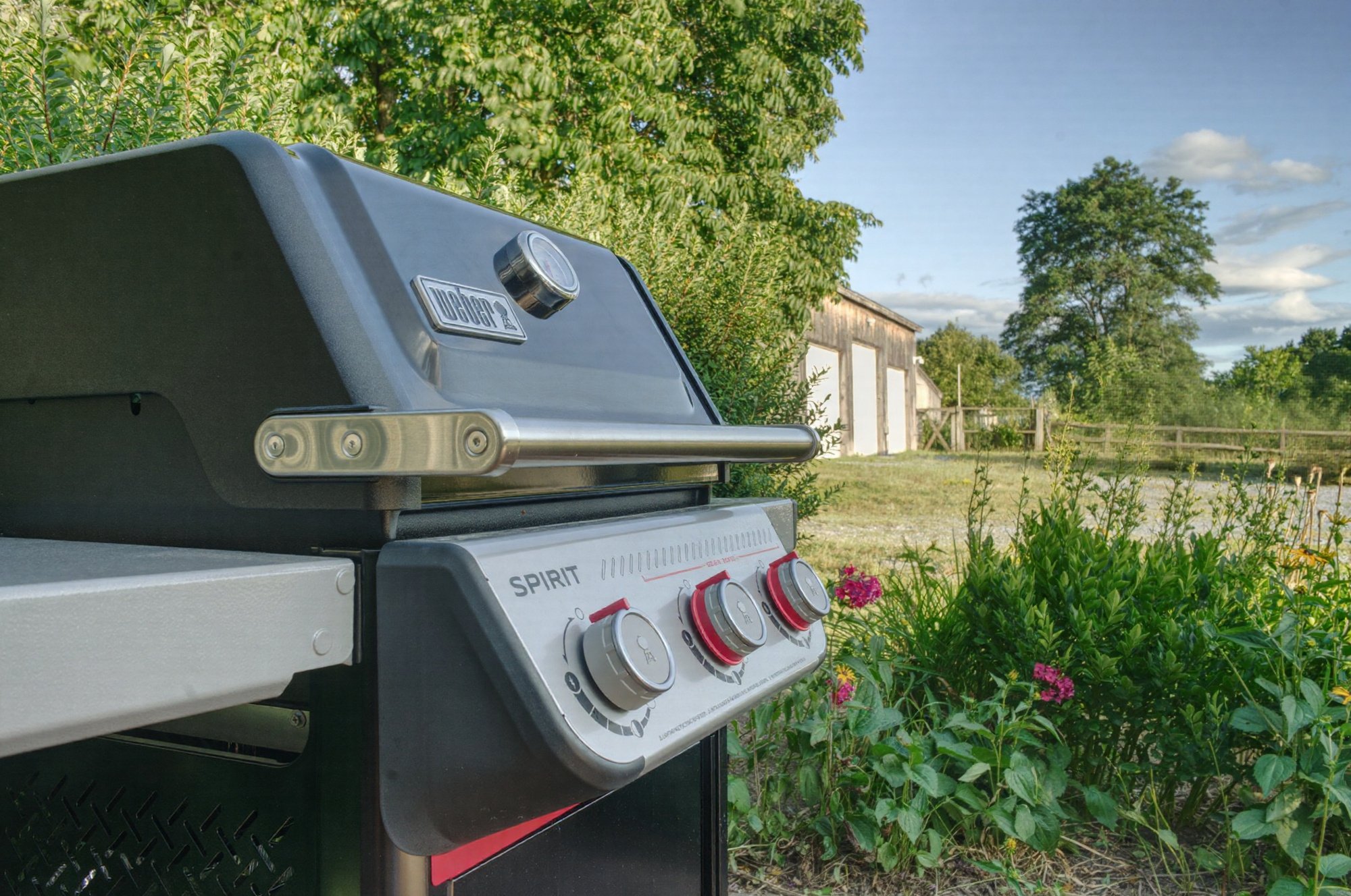 Gas grill on the guest house patio surrounded by gardens, with the barn and countryside beyond.